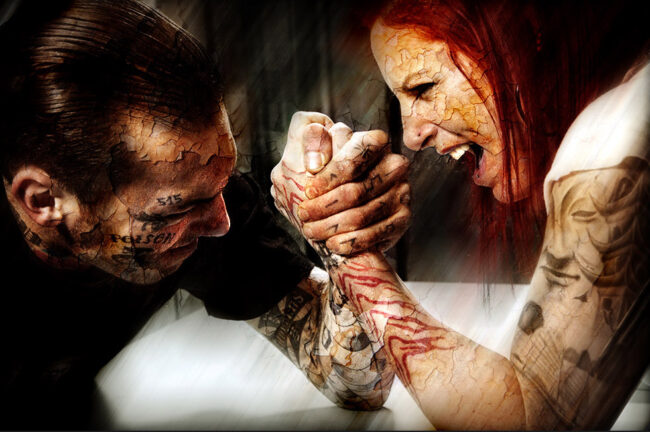 Une homme et un femmes aux visages craquelés font un bras de fer