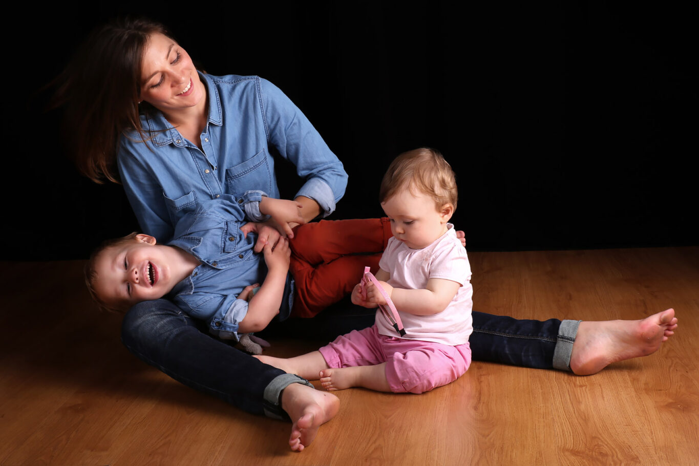 Une maman assise sur le parquet du studio photo s'amusent avec ses deux enfants
