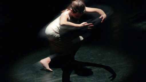 Une femme en robe blanche danse gracieusement dans l'obscurité sur un parquet sombre