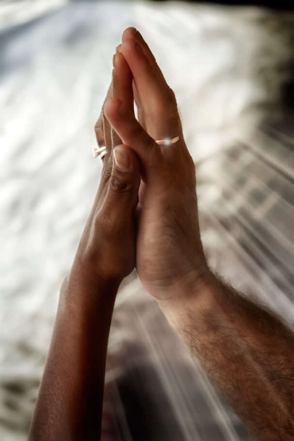 Deux mains d'origine ethnique différente, avec des anneaux de fiançailles en gros plan, s’enlacent l'une contre l'autre.