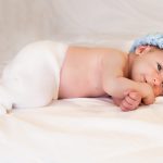 un bébé avec un bonnet bleu sur la tête est allongé sur une couette blanche