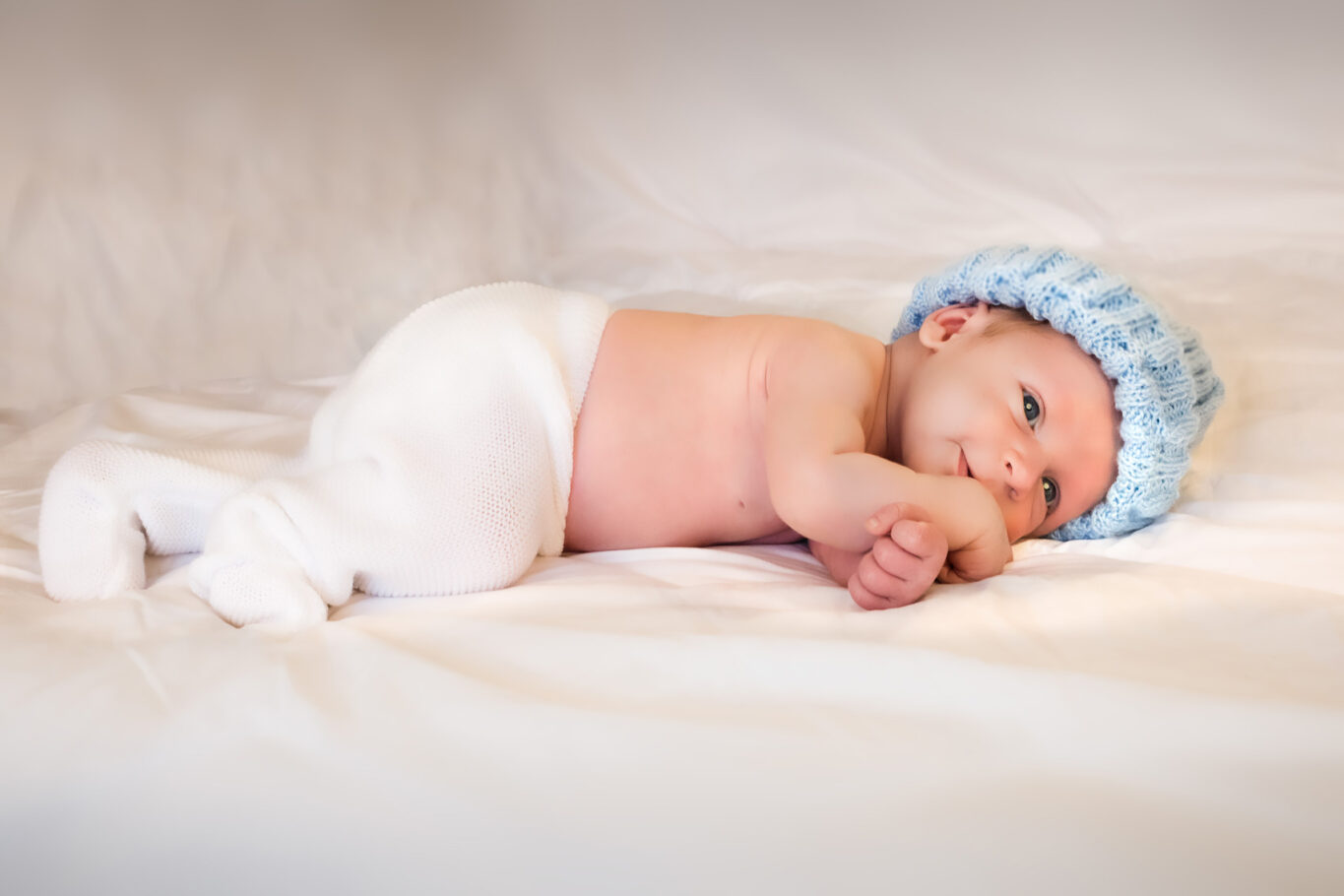 Un petit bébé allongé sur le ventre regarde vers l'objectif photo et sourit