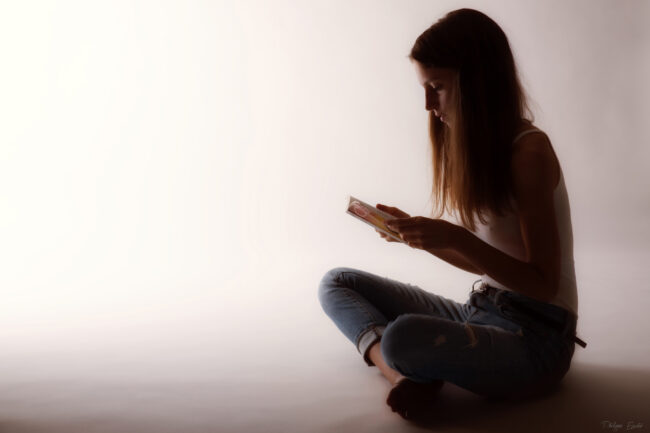 Modèle photo assise en tailleur en semi pénombre, captivée par la lecture d'un livre.