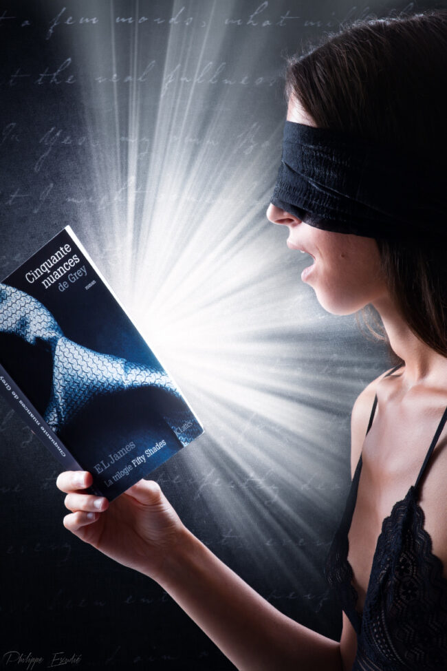 Modèle photo en nuisette, un livre à la main, bouche entrouverte avec un grand éclat de lumière derrière elle.