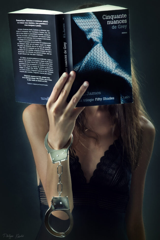 Un modèle photo, bras menoté, tient le livre 50 nuances de grey qui lui cache le visage.