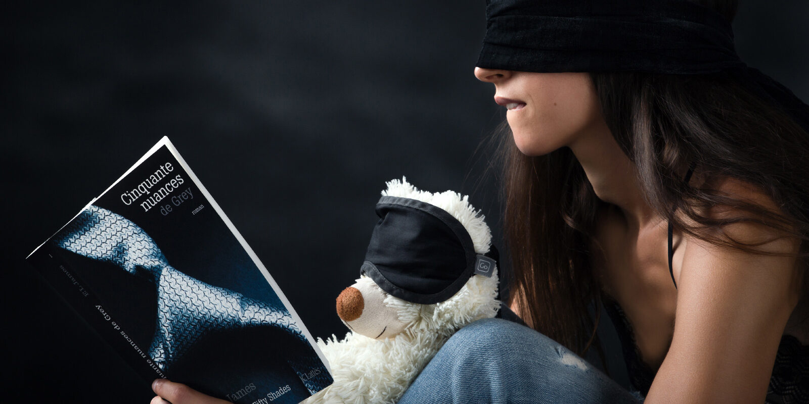 Un ours en peluche et un modèle photo, les yeux bandés, semblent apprécier le livre 50 Nuances de grey.