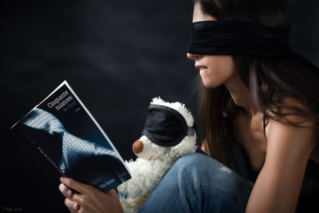 Un ours en peluche et un modèle photo, les yeux bandés, semblent apprécier le livre 50 Nuances de grey.