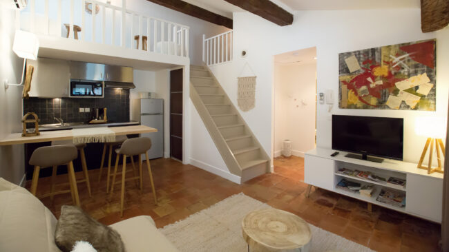 Intérieur d'un salon avec télé, canapé et cuisiné entièrement équipée.