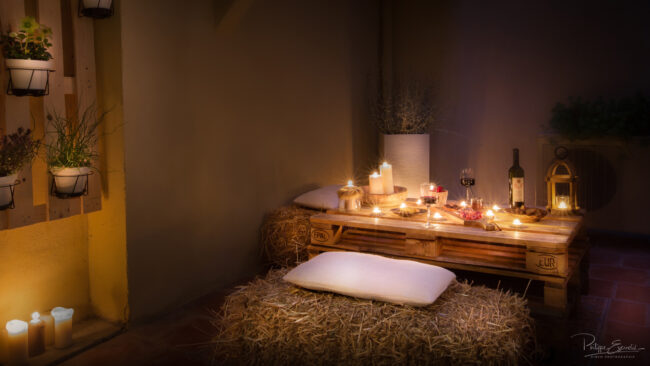 Plan large de l'apéritif servi de nuit en terrasse avec bougies, vin et charcuterie.