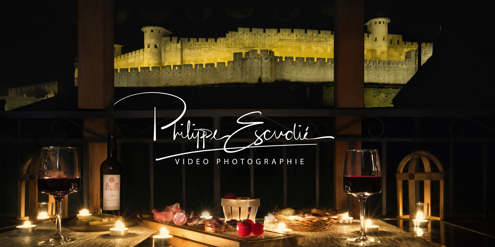 Ambiance apéritif de nuit sur une terrasse d'appartement, vin, charcuterie, bougie et la Cité de Carcassonne comme décor.
