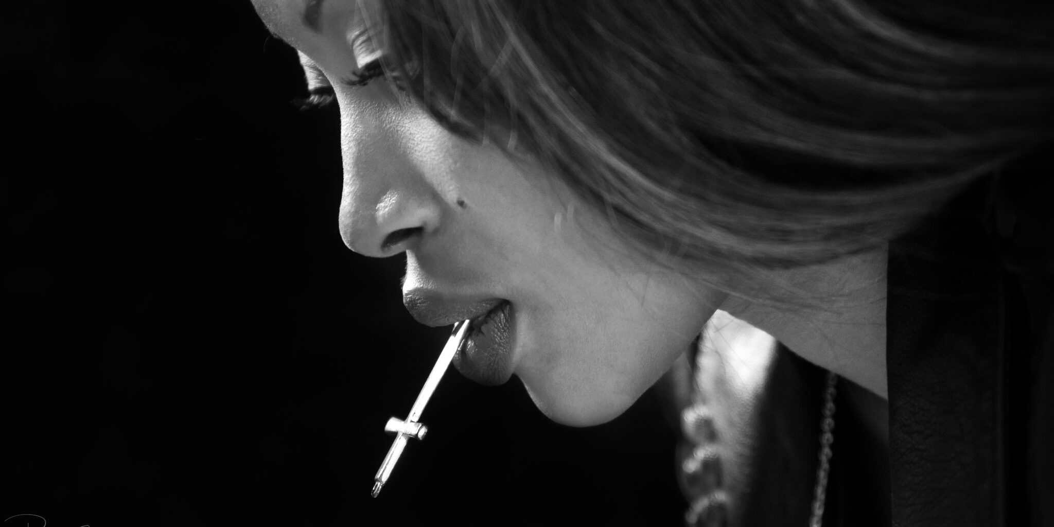 Gros plan du visage du modèle photo Nina, en noir et blanc, tenant une croix d'argent dans sa bouche