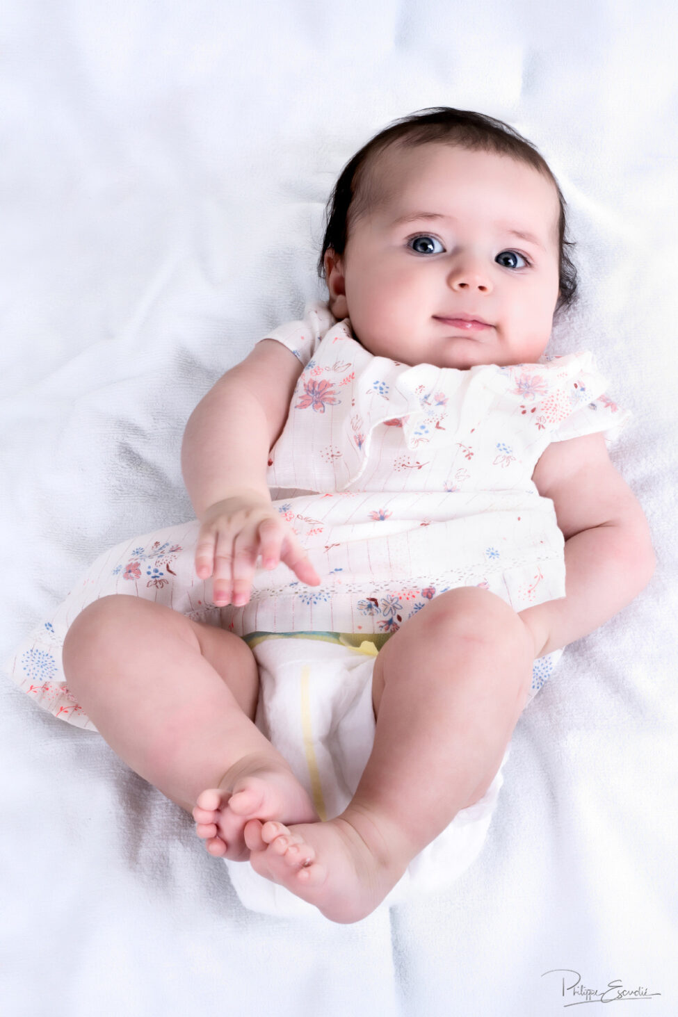 Bébé souriant à l'objectif, allongé sur le dos sur un linge blanc.