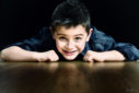 Petit garçon allongé sur le parquet du studio photo, le regard fixant l'objectif avec un grand sourire.