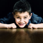 Petit garçon allongé sur le parquet du studio photo, le regard fixant l'objectif avec un grand sourire.