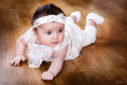 Bébé allongé sur sur le ventre, tête redressée, sur le parquet du studio photo