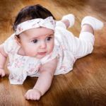 Bébé allongé sur sur le ventre, tête redressée, sur le parquet du studio photo