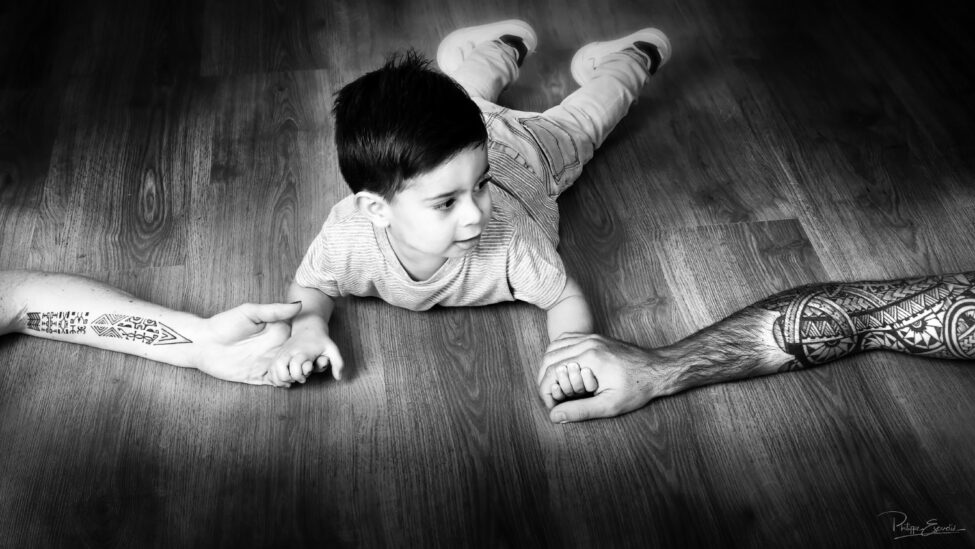 Manao, petit garçon tenant les bras tatoués de son papa et sa maman.