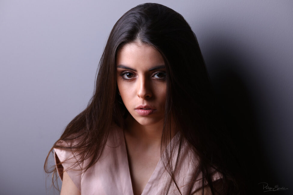 Shooting book photo de Jenny au studio de Carcassonne 2 Regard intense de jenny, bouche entrouverte, cheveux tombant sur les épaules, assise contre un mur gris.