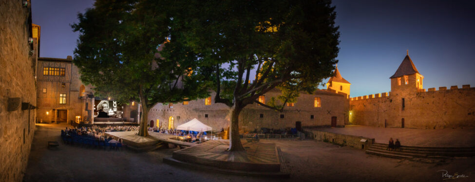Vue panoramique de la Cour intérieure du Château Comtal de la Cité de Carcassonne lors de la projection nocturne sur grand écran d'un documentaire devant un vaste public assis.