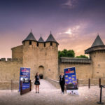 Devant le pont du Chateau Comtal de la Cité de Carcassonne, deux hôtesses d'accueil sourient avec de part et d'autre deux affiches du festival Contrechamps