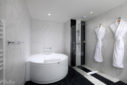 Salle de bain en marbre de l'hôtel Hilton de Carcassonne avec une grande baignoire, une douche et deux peignoirs blancs