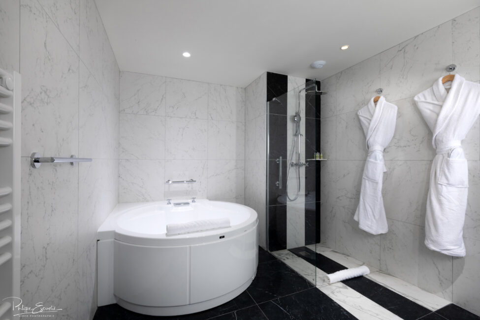 Salle de bain en marbre de l'hôtel Hilton de Carcassonne avec une grande baignoire, une douche et deux peignoirs blancs