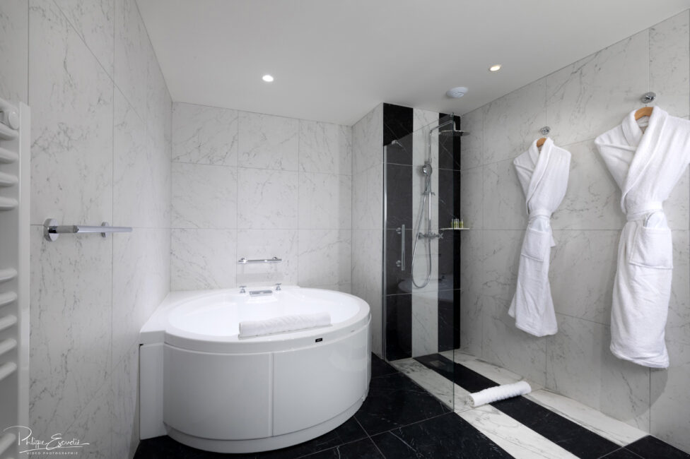 Salle de bain en marbre de l'hôtel Hilton de Carcassonne avec une grande baignoire, une douche et deux peignoirs blancs
