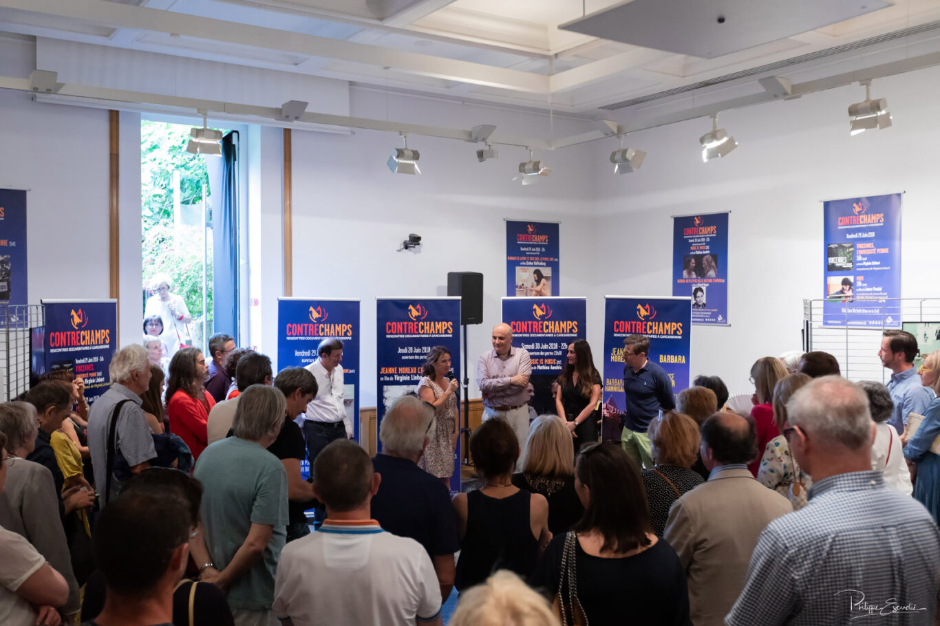 Une réalisatrice micro à la main en plein jour dans une salle remplie d'invités présente son film