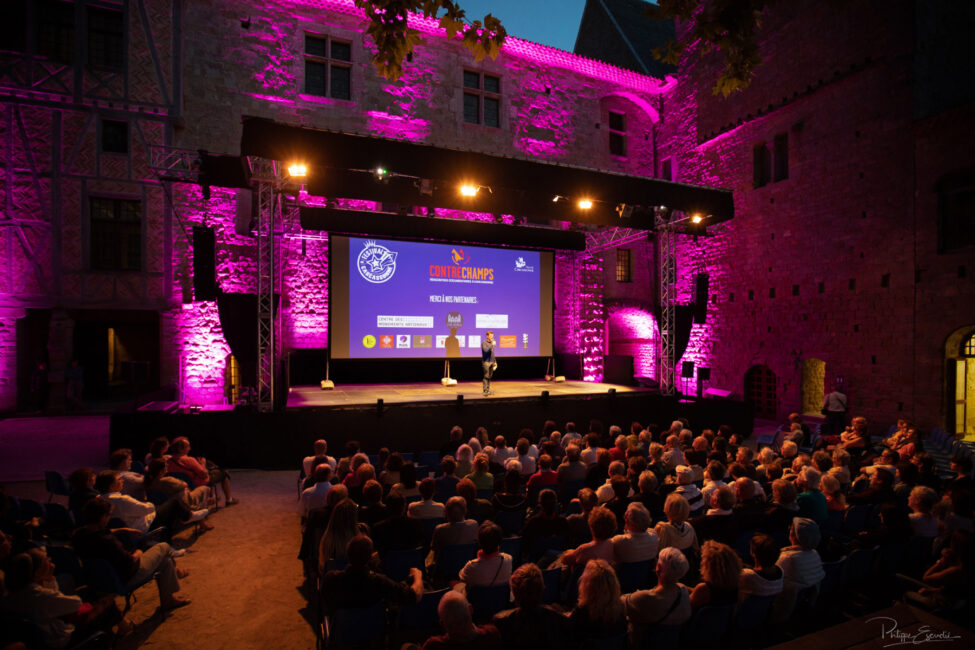 Yves jeuland sur scène un micro à la main face à un nombreux public assis en extérieur dans la cour du midi du Château Comtal de carcassonne