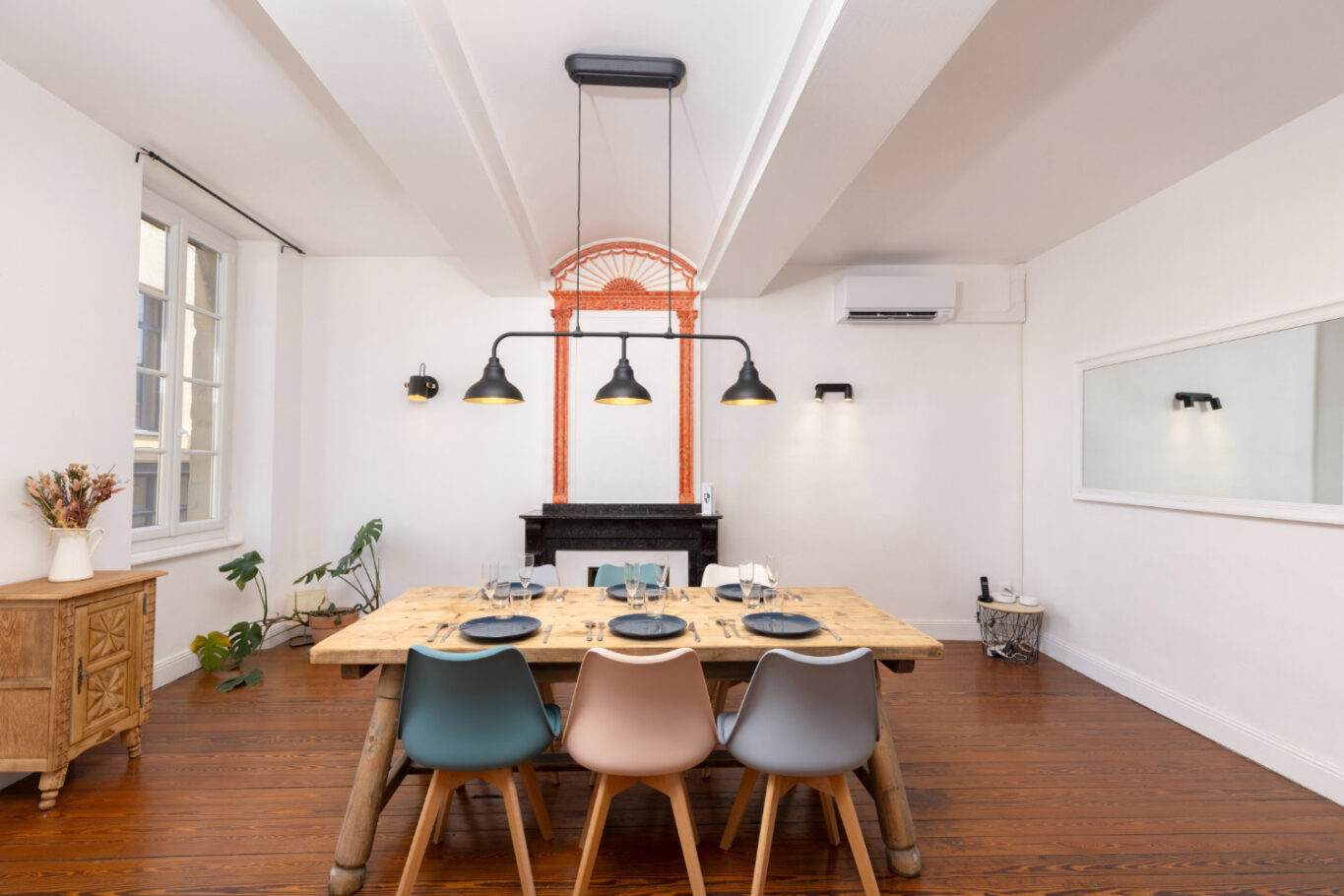 Élégante salle à manger avec un parquet en bois, une grand table en bois dressée et une rampe de luminaires au dessus de la table.