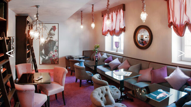 Salle décorée en rose et violet, comprenant des canapés et des tables, offrant un espace convivial et stylé.