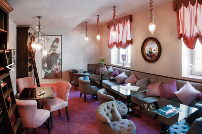 Salle décorée en rose et violet, comprenant des canapés et des tables, offrant un espace convivial et stylé.