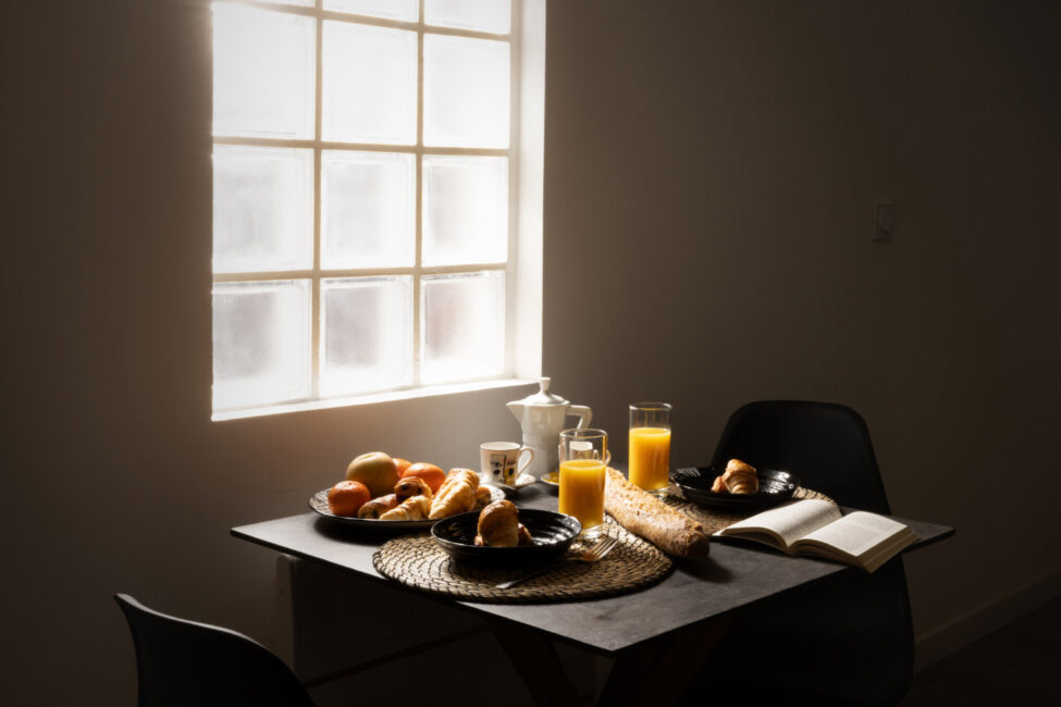 un petit déjeuner avec viennoiseries et jus d'orange sur une table éclairée par la lumière diffuse d'une fenêtre