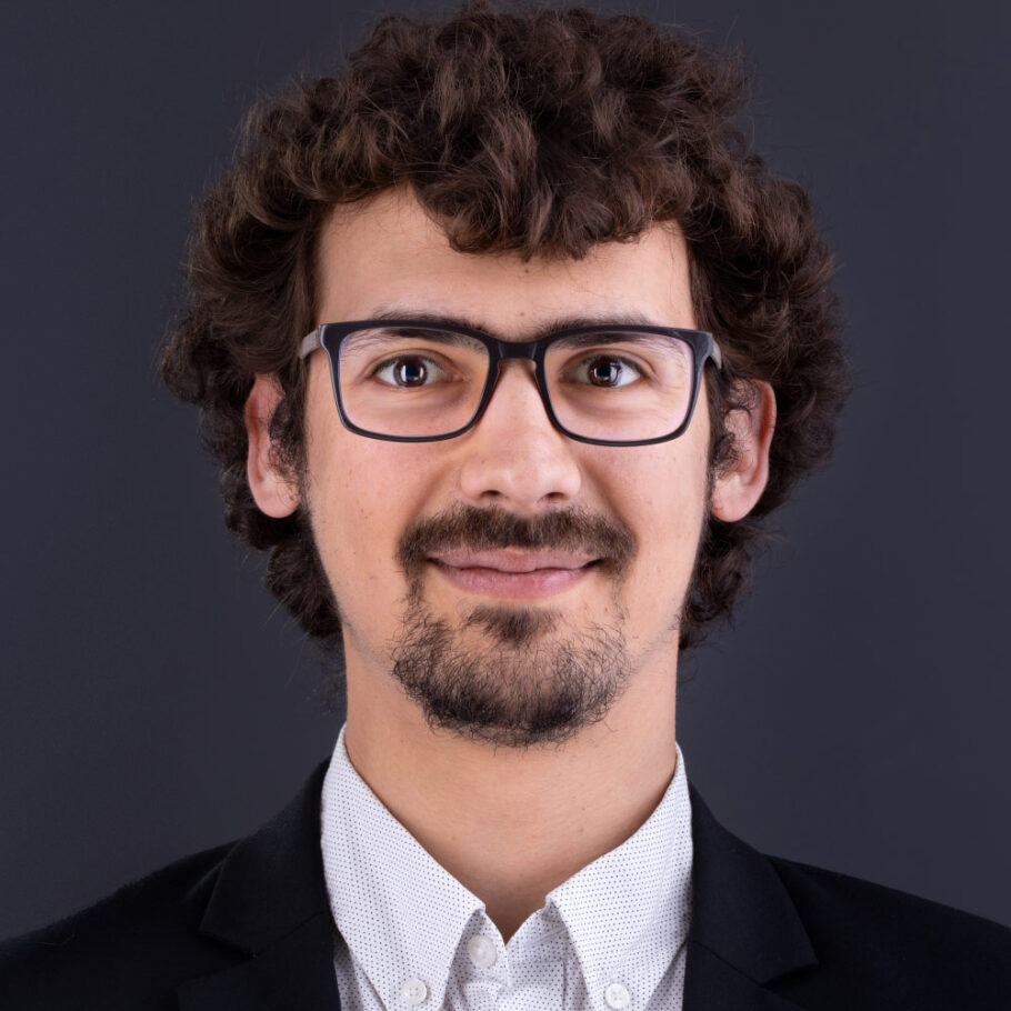 Un homme portant des lunettes, souriant face camera, en chemise blanche et veste noire