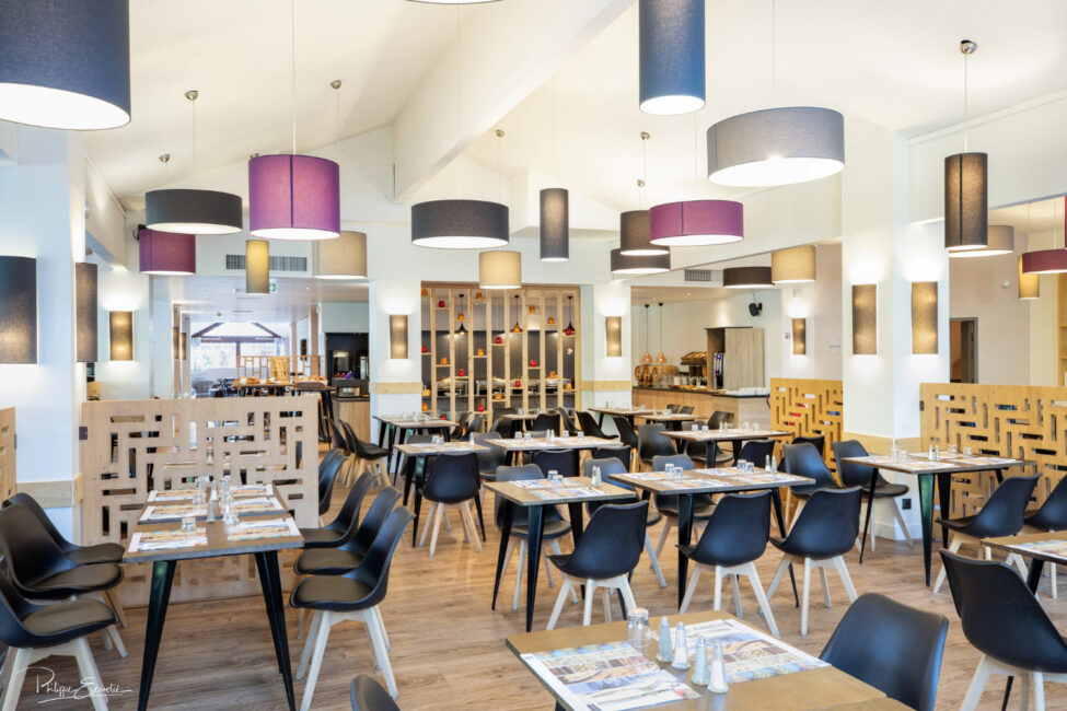 salle de restaurant avec des tables dressées, des chaise et de nombreux luminaires au plafond