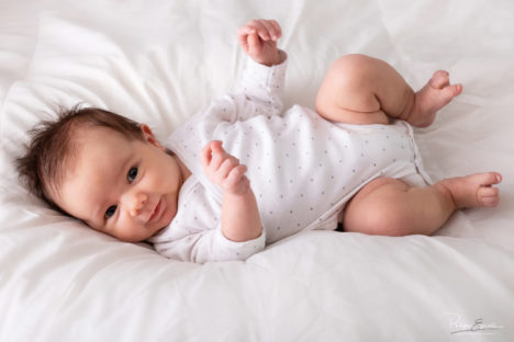 Regard fixe d'un bébé allongé en entier sur une couette blanche