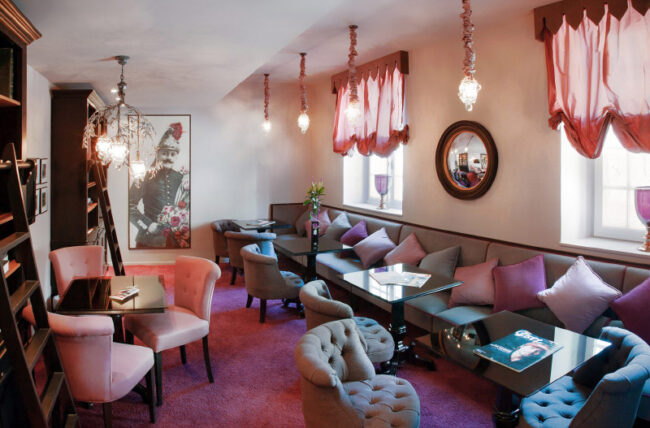 salon en rose et violet avec moquette, comprenant des canapés et des tables, offrant un espace convivial et stylé.