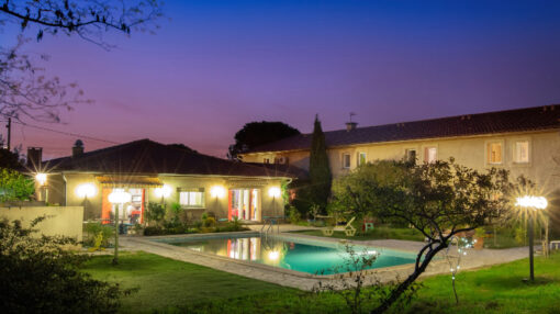 Vue nocturne d'une maison avec piscine, illuminée, évoquant une ambiance tranquille et charmante.
