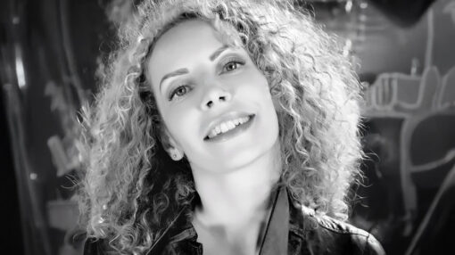 portrait noir et blanc d'une femme souriante aux long cheveux bouclé tenant une ceinture dans sa main