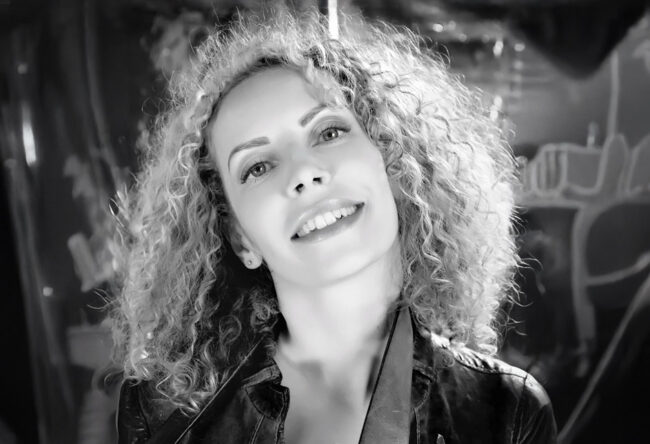 portrait noir et blanc d'une femme souriante aux long cheveux bouclé tenant une ceinture dans sa main