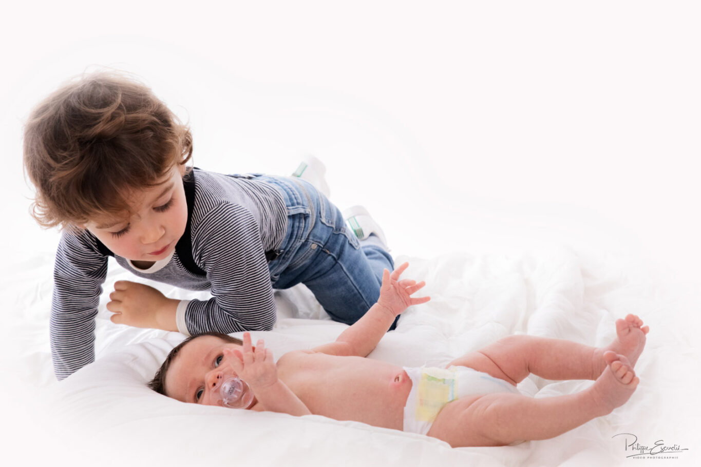 Un enfant rejoint sur un lit un bébé allongé, une sucette à la bouche