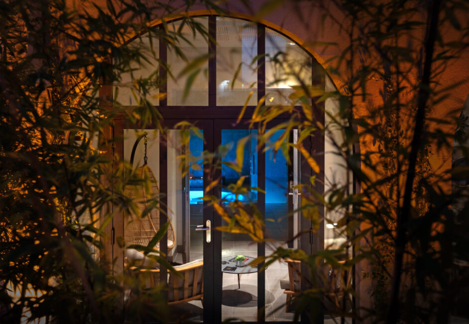 végétation avec en arrière-plan une porte vitrée et un spa allumé avec des spots bleus