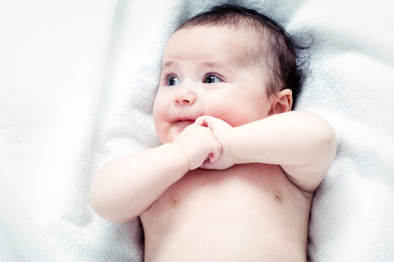 un bébé allongé sur le dos sur une couette blanche les bras croisés