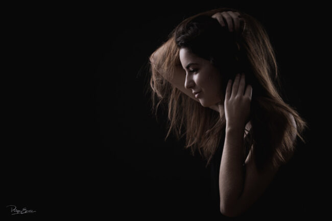 Plan serré de trois quart d'une fille souriante, les mains dans les cheveux