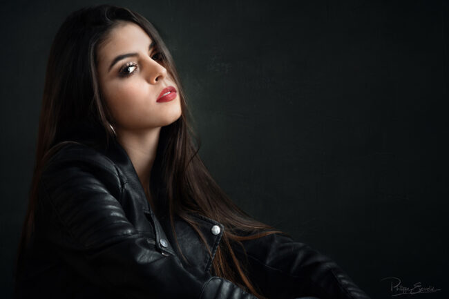 une jeune fille assise avec des cheveux longs et un blouson de cuir