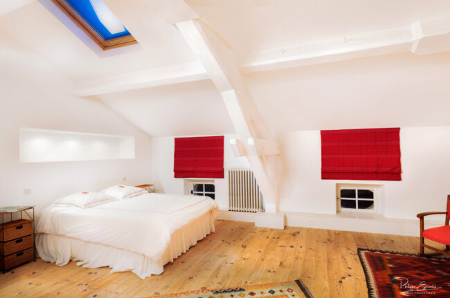 Photos immobilières du mois 3 Grande chambre de type loft, avec de grands murs blancs, un parquet en bois et des rideaux rouges.
