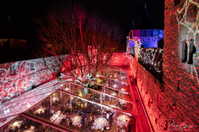 Tables dressées sous un immense chapiteau transparent avec des murailles médiévales tout autour eclairéées de rouge