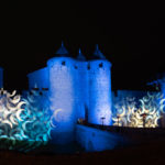 Projection de nuit de formes en demi-lune sur les murailles du château comtal éclairées en bleu