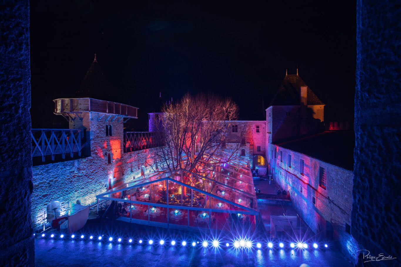 vue en plongée du château comtal de nuit avec dans la cour du midi un chapiteau transparent et des tables dressées à l'intérieur.