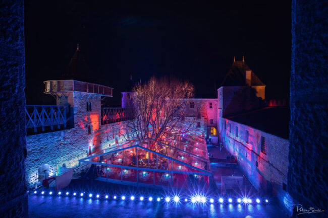 vue en plongée du château comtal de nuit avec dans la cour du midi un chapiteau transparent et des tables dressées à l'intérieur.